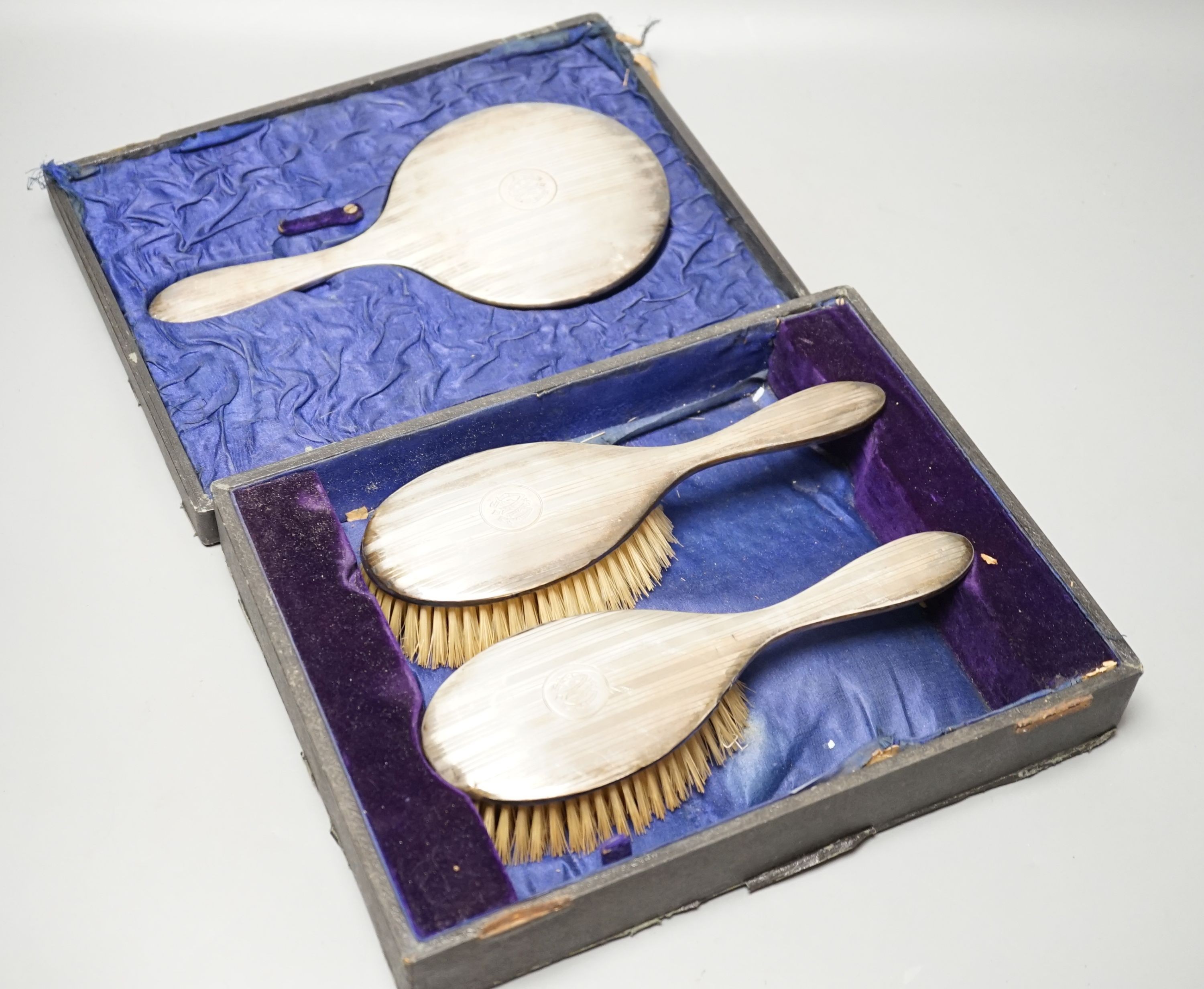 A cased George V three piece silver mounted dressing table set, including a mirror and two brushes.